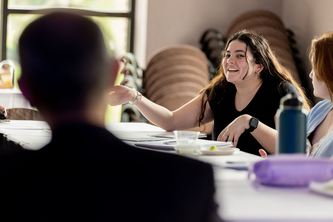 A college student with dark hair smiles as she asks a question of novelist Mohsin Hamid